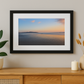Framed artwork of a sunset over water on a wall above a wooden console table with decorative items.