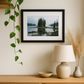 Framed landscape print on a wall above a wooden cabinet with decorative items.