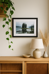 Framed landscape print on a wall above a wooden cabinet with decorative items.